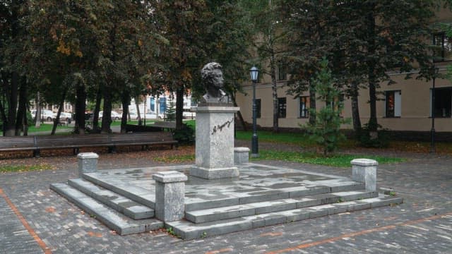 Bust statue of Pushkin in a park surrounded by trees on a cloudy day
