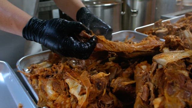 Preparing boiled meat on a metal tray with gloved hands