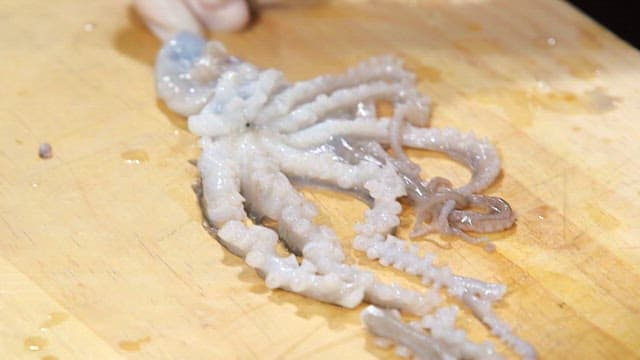Live octopus being cut with a knife on a wooden cutting board