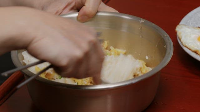Stirring rice and fried eggs with a spoon in a brass bowl