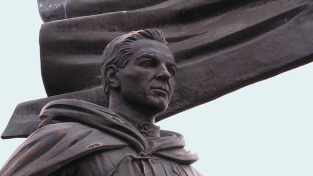Historical statue of a man with a cloak under a cloudy sky