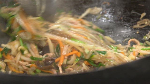 Stir-frying glass noodles, vegetables, and meat in a hot wok