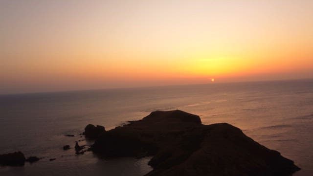 Sunset over a calm ocean with rocky cliffs