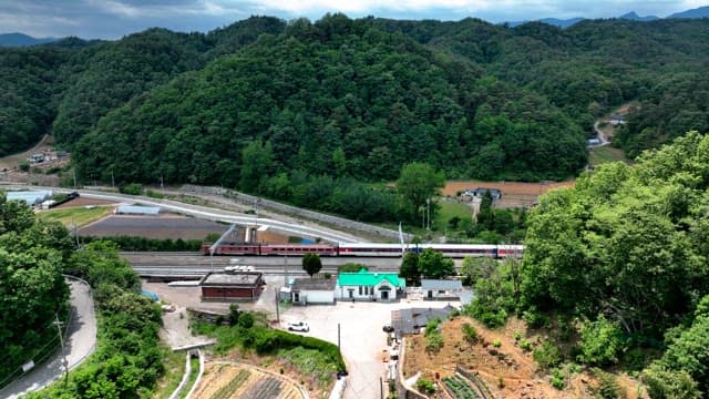 Small countryside train station nestled in lush green hills under a cloudy sky