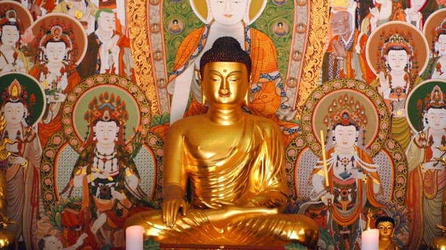 Golden Buddha statue surrounded by intricate and colorful religious paintings