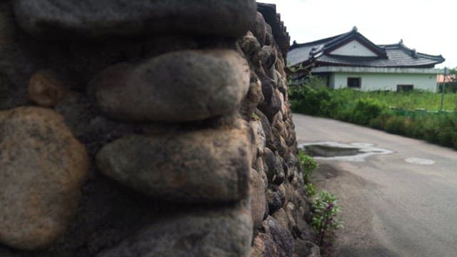 Tranquil village road flanked by an old stone wall and a traditional house