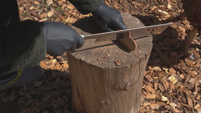 Person cutting wood on a stump outdoors