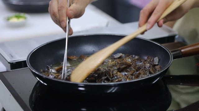 Stir-frying the half-dried saury with a wooden spatula in an oiled frying pan