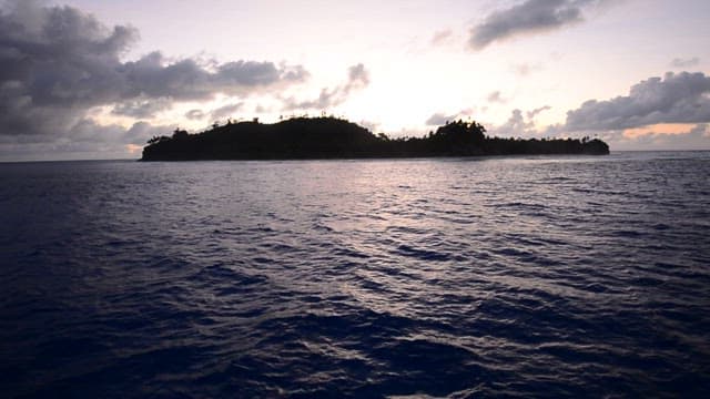 Sunset over a tranquil island in the ocean with clouds gathering.