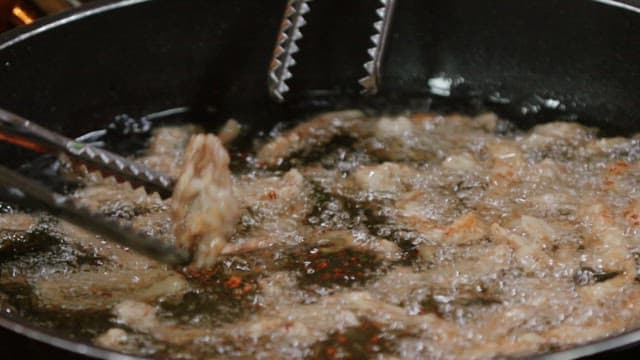 Stirring meat being fried in a frying pan with tongs