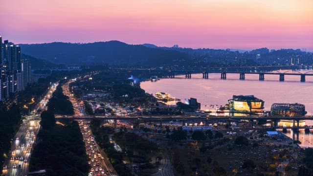 Evening cityscape by a river with heavy traffic and illuminated buildings