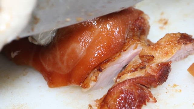 Pig's feet being cut with a knife on a cutting board in the kitchen