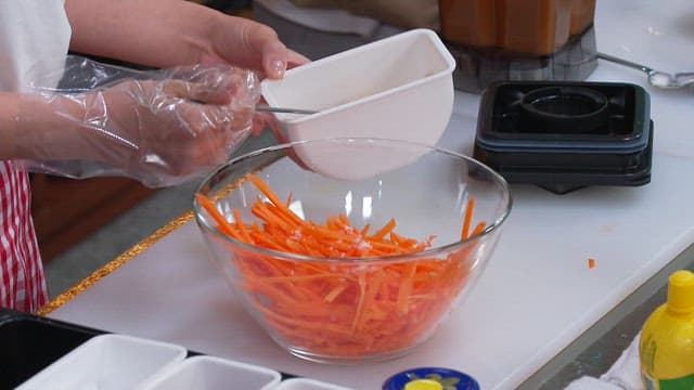 Seasoning Shredded Carrots in a Glass Bowl