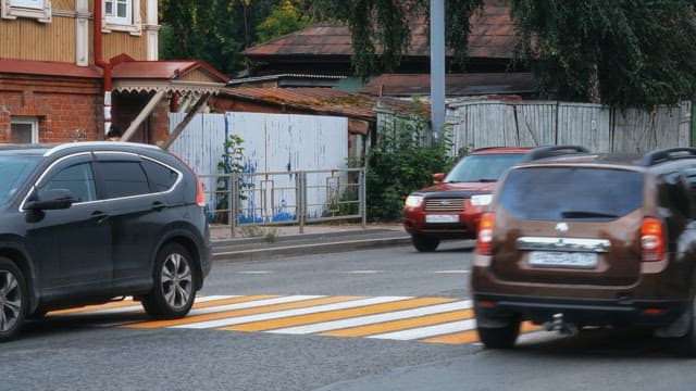 Cars passing by a pedestrian walking past an old building in the city during daytime