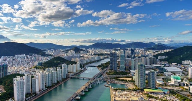 Mountains, rivers, and urban buildings under a blue sky with flowing clouds