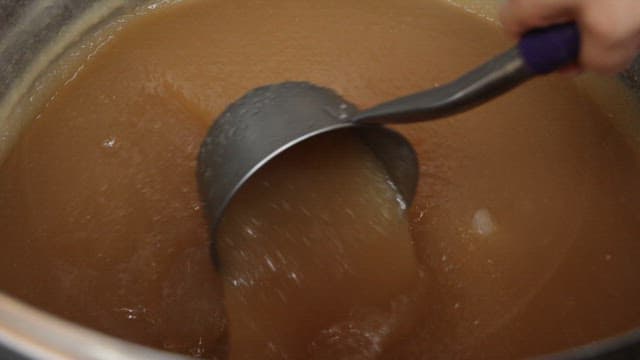 Ladling broth with floating ice cubes from a large pot