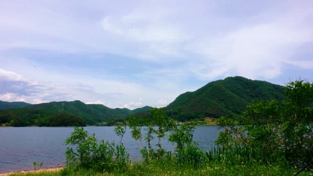 Serene lake surrounded by green hills under a cloudy sky