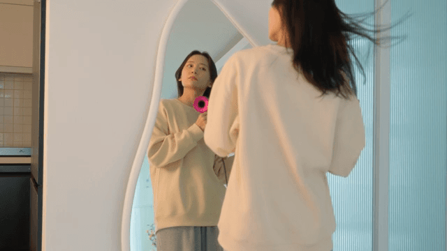 Woman drying her hair with dryer in front of a mirror