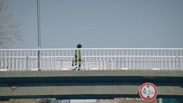 Person walking alone on a bridge under a clear sky