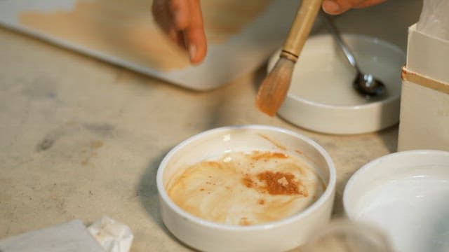 Hands preparing pigments in a ceramic dish for painting
