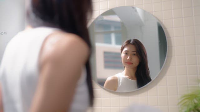 Woman drying her hair with a towel in front of a bathroom mirror