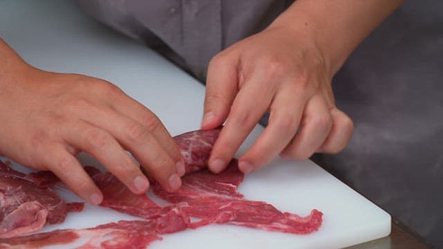 Hands rolling slices of beef with green onions on a cutting board
