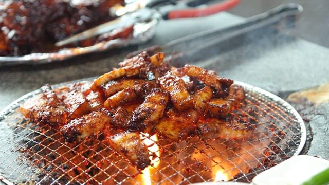 Chopstick of meat sizzling on a grill over blazing charcoal