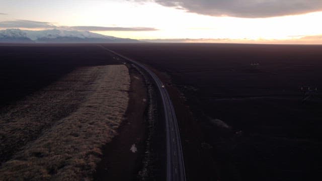 Car driving on a long road under a sunset sky