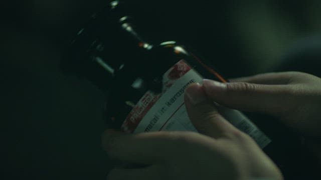 Hands examing a glass bottle containing sodium metal at night
