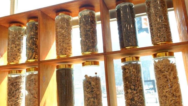 Rows of jars filled with various dried herbs on a wooden shelf