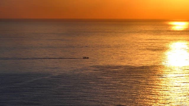 Boat sailing on a golden sea at sunset