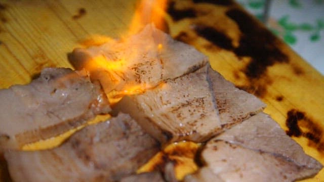 Slices of meat being torched on a board
