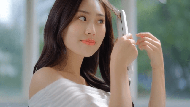 ㅉoman styling her hair with hair straightener indoors near a window