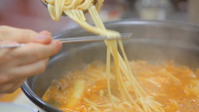 Noodles picked from the spicy noodle soup with chicken boiling in the pot