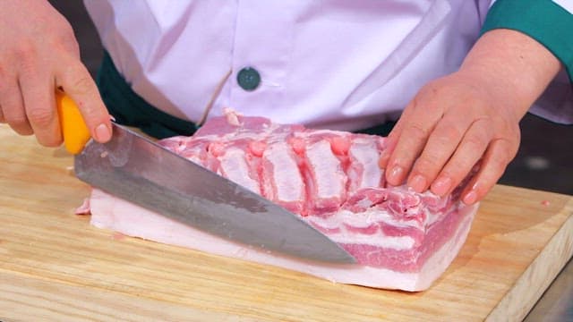 Chef cutting whole pork belly with a knife