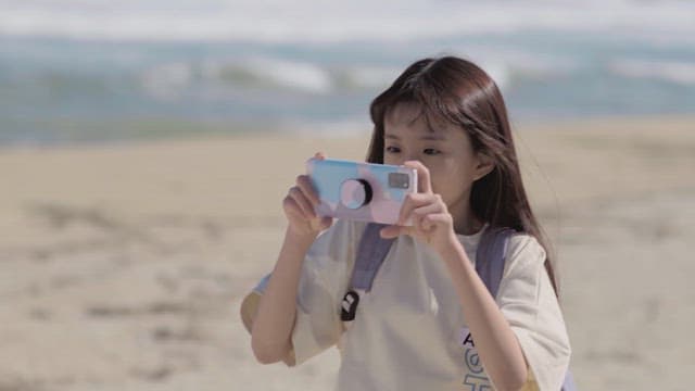 Young girl on the beach taking a photo with her phone