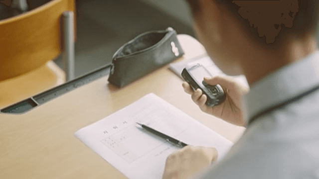 Student Answering Phone While Writing at Desk