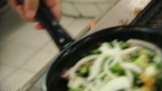 Pouring the spicy sauce into a pan with various vegetables and sand eels in the kitchen