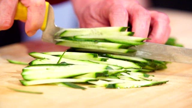 Slicing fresh cucumbers on a wooden cutting board