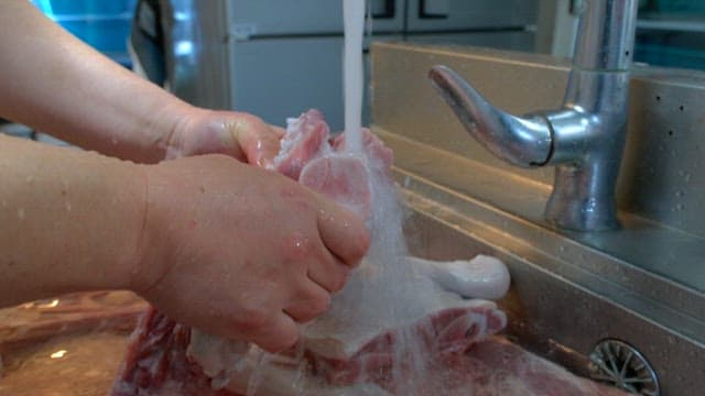 Washing large cuts of raw meat under running water in a kitchen