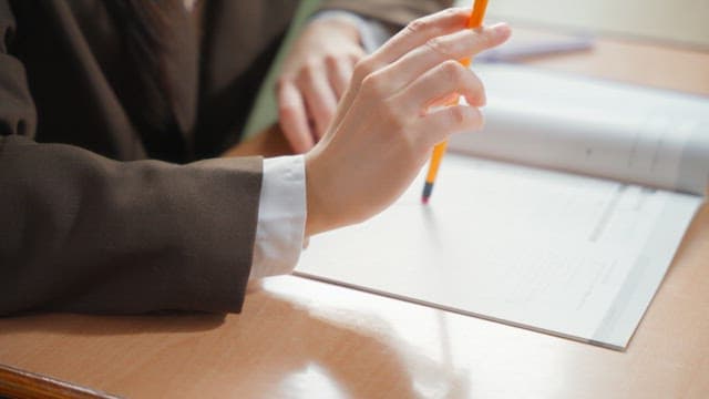 Student sharpening a pencil with a knife on a book