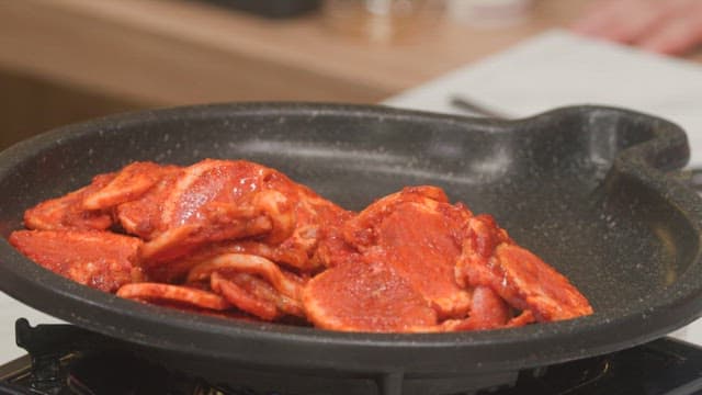 Slices of marinated meat being placed in a hot pan