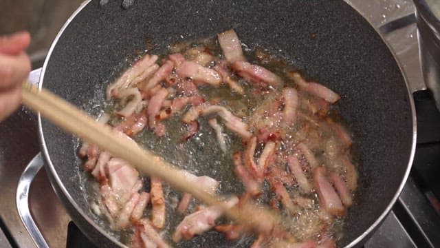 Sizzling bacon being cooked in an oiled frying pan