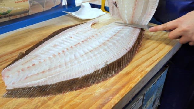 Flounder being prepared on a wooden cutting board at a fish market