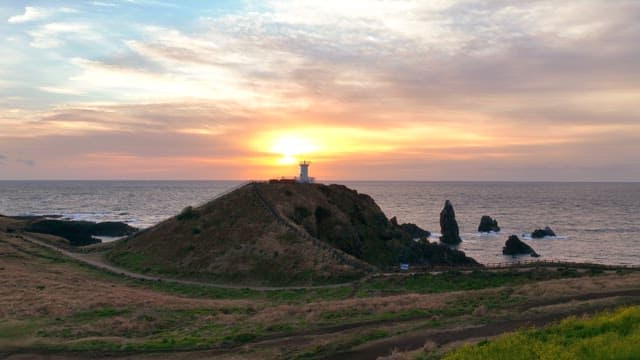 Lighthouse on a hill at sunset by the sea