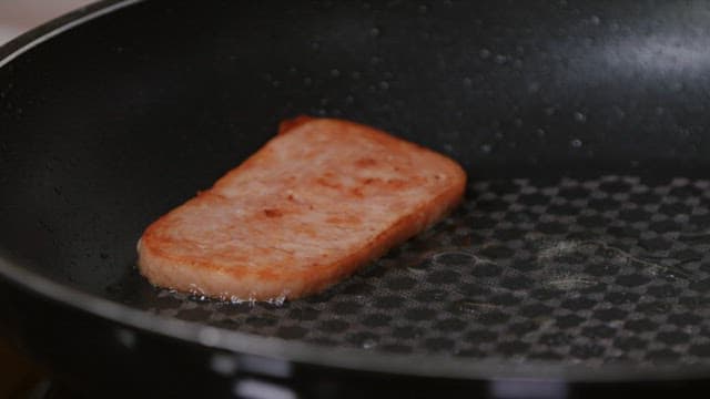 Plating fried spiced ham slices on a frying pan using wooden spatulas