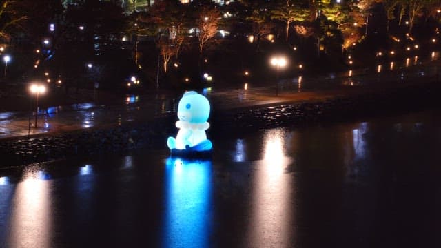 Brightly lit statue by a river at night with reflections