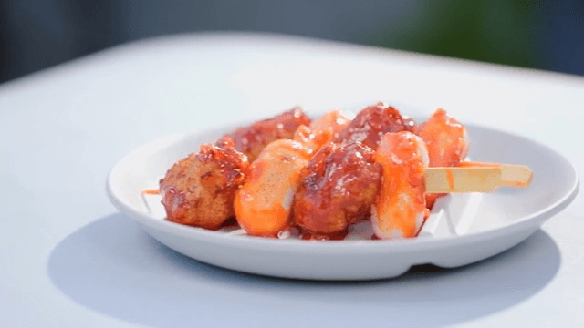 Fried fish and rice cake skewers with spicy sauce served on a white plate