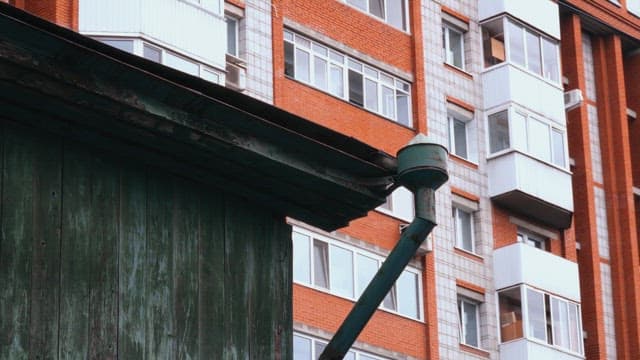 An old green wooden building below a modern red brick apartment complex.