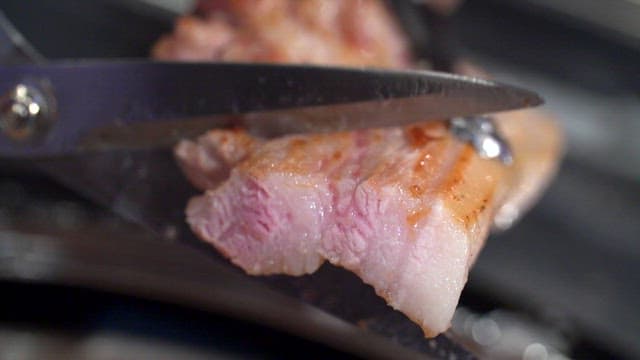 Grilled pork belly being cut with scissors